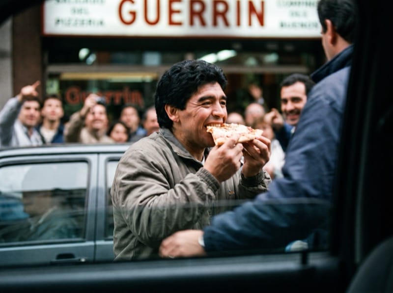 Diego comiendo una porción en la vereda de una pizzería