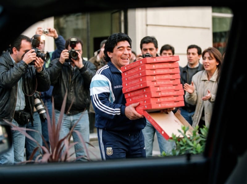 Diego cargando cajas de pizza entre fotógrafos