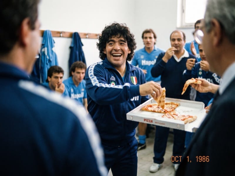 Diego sonriendo con una pizza en la mano y sus compañeros atrás